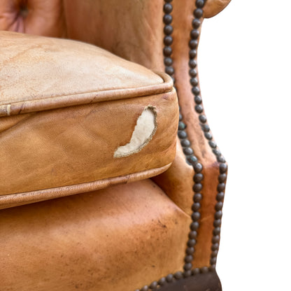 Tan leather wingback chair showing rolled arm and studded trim along the wing