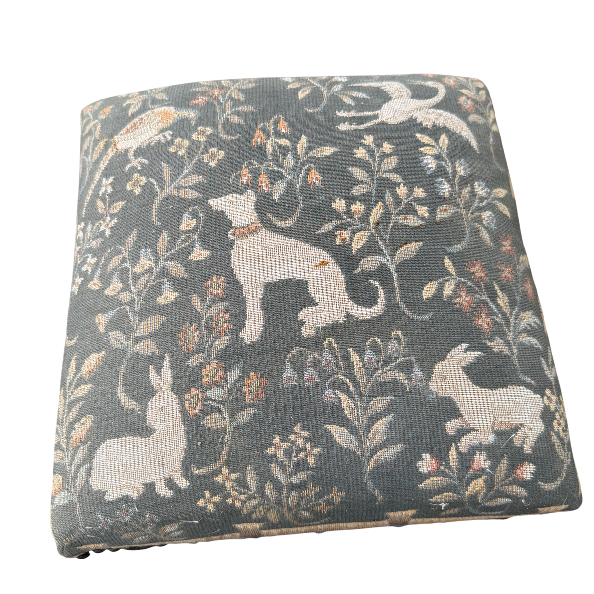 Corner view showing studded trim and tapestry pattern on upholstered footstool