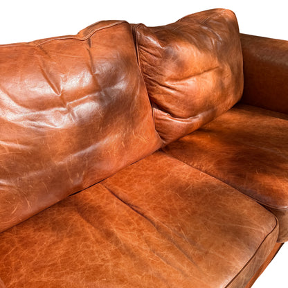 Two-seater tan leather sofa with sturdy frame and removable feet visible