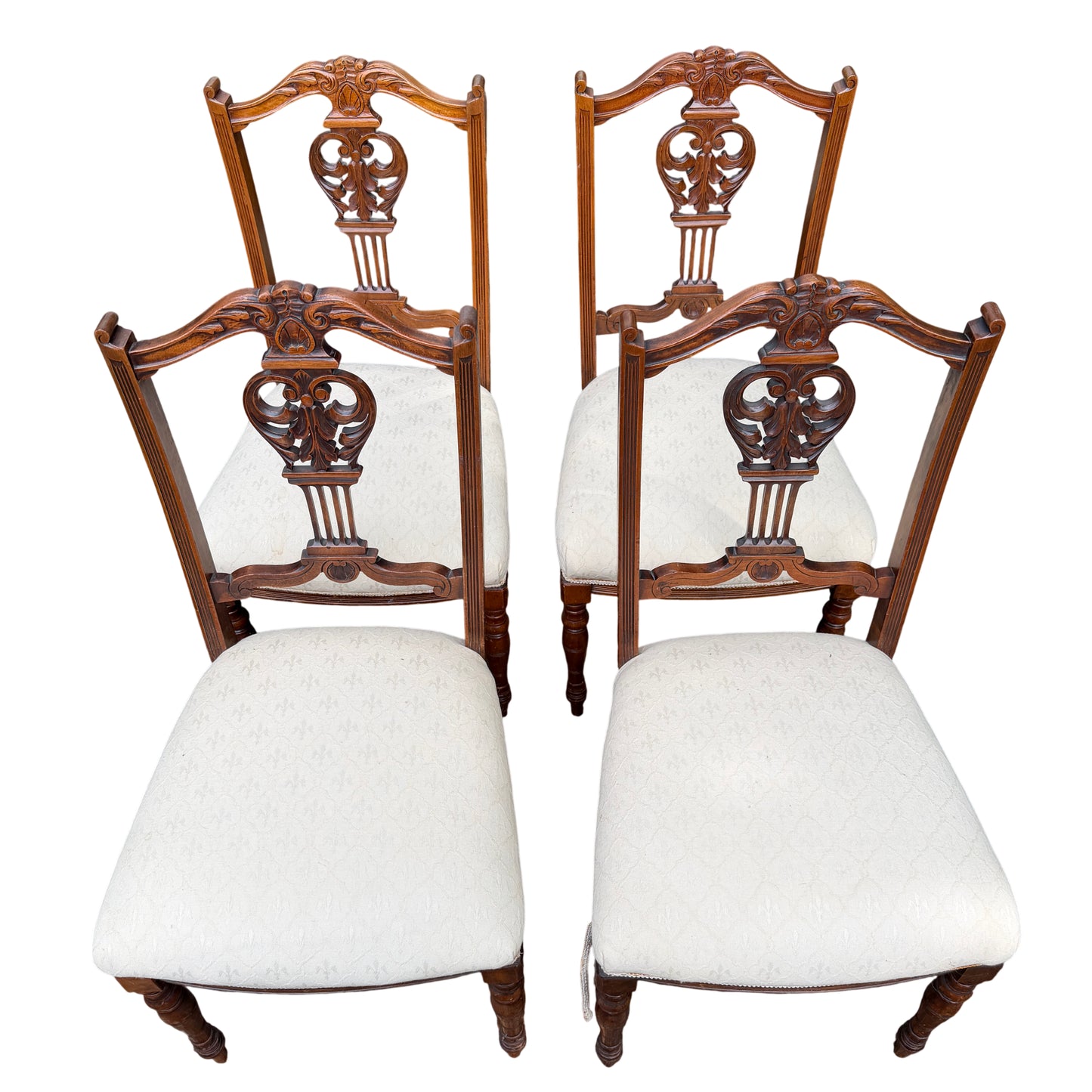 Front view of set of four wooden dining chairs with carved backs and cream seats