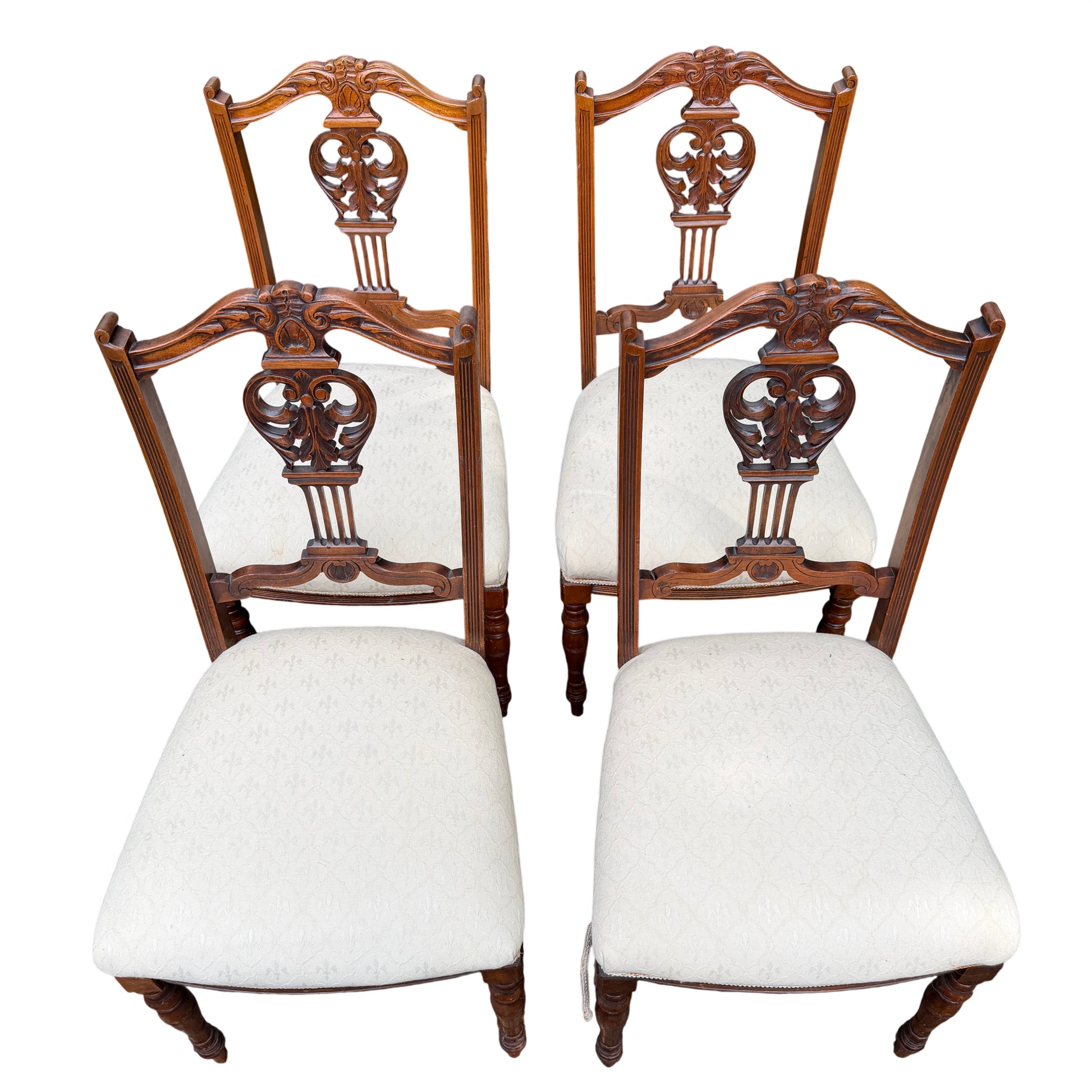 Front view of set of four wooden dining chairs with carved backs and cream seats
