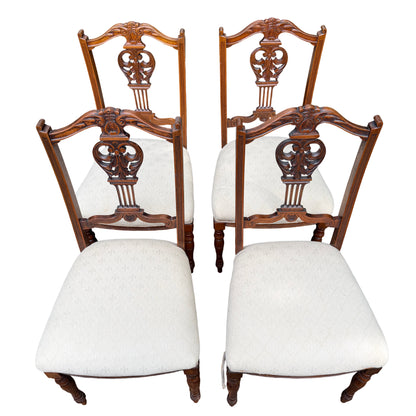 Front view of set of four wooden dining chairs with carved backs and cream seats