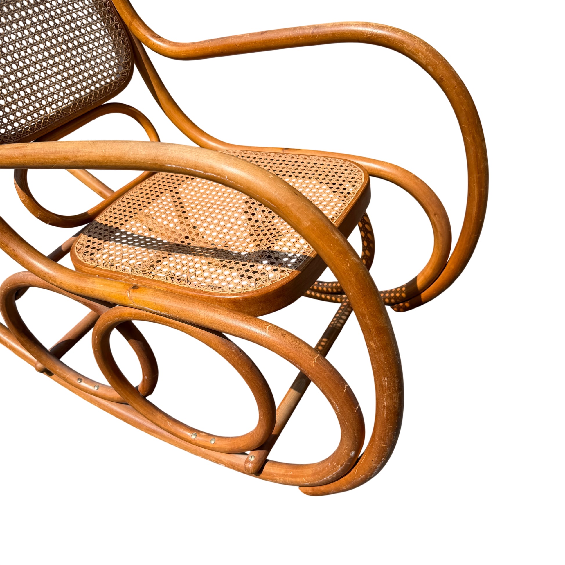 Close-up showing holes and wear to the cane on the seat of the rocking chair