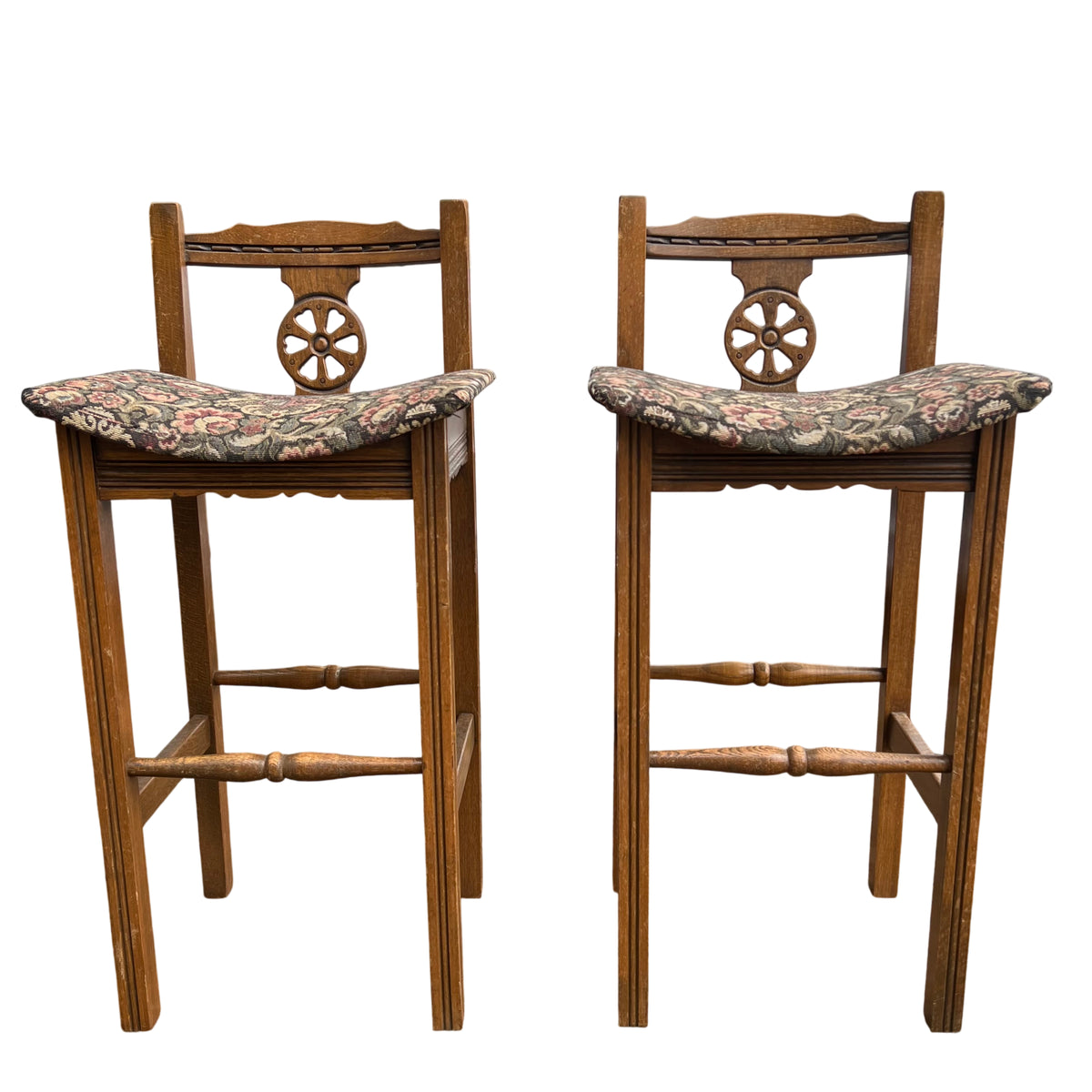 Front view of two Old Charm oak bar stools showing carved wheel back splats and upholstered seats