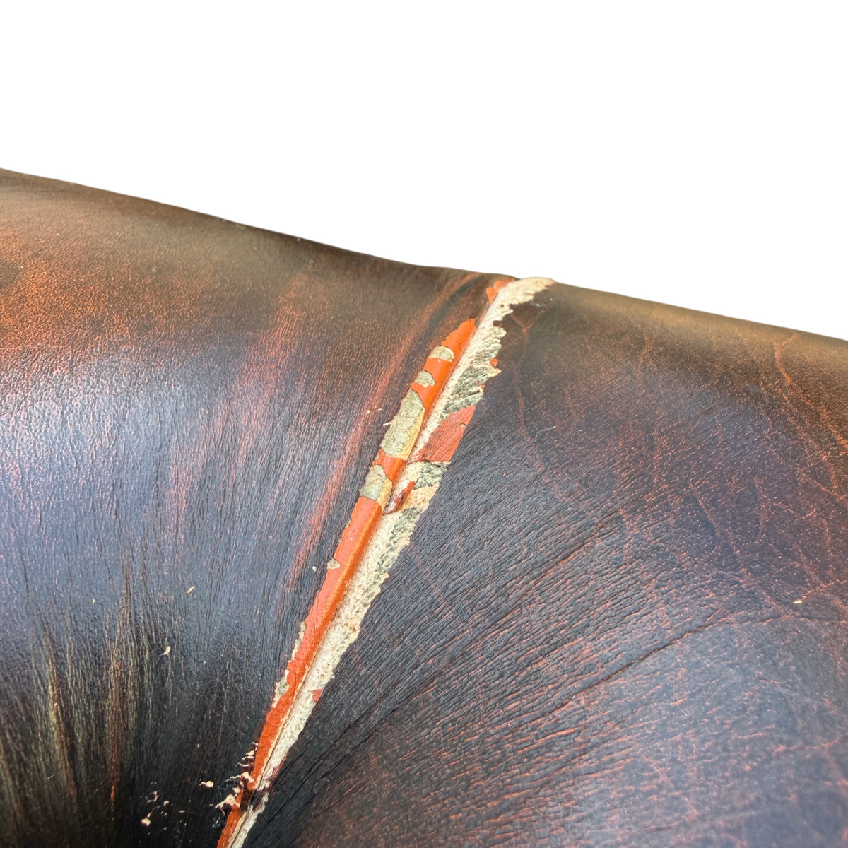 Side view showing distressed brown leather and scuffed base of Chesterfield armchair