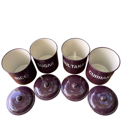 Row of four labelled enamel canisters on wooden sideboard in outdoor setting