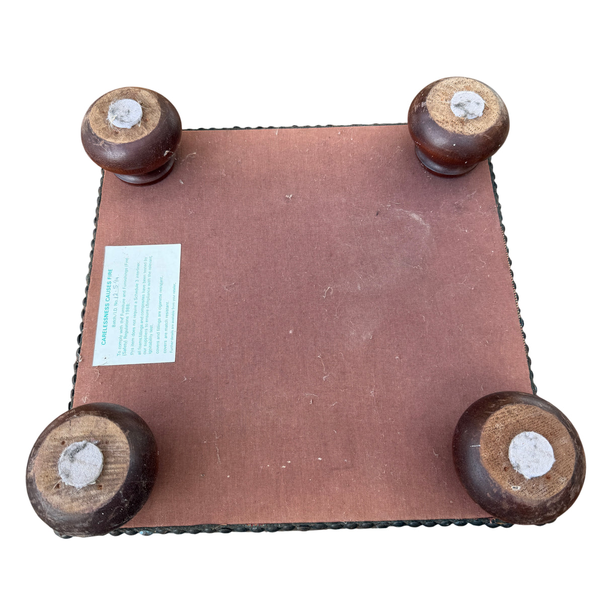 Side profile of compact upholstered footstool with turned wooden feet