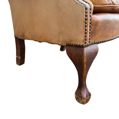 Three-quarter view of vintage leather wingback chair showing buttoned back and studding