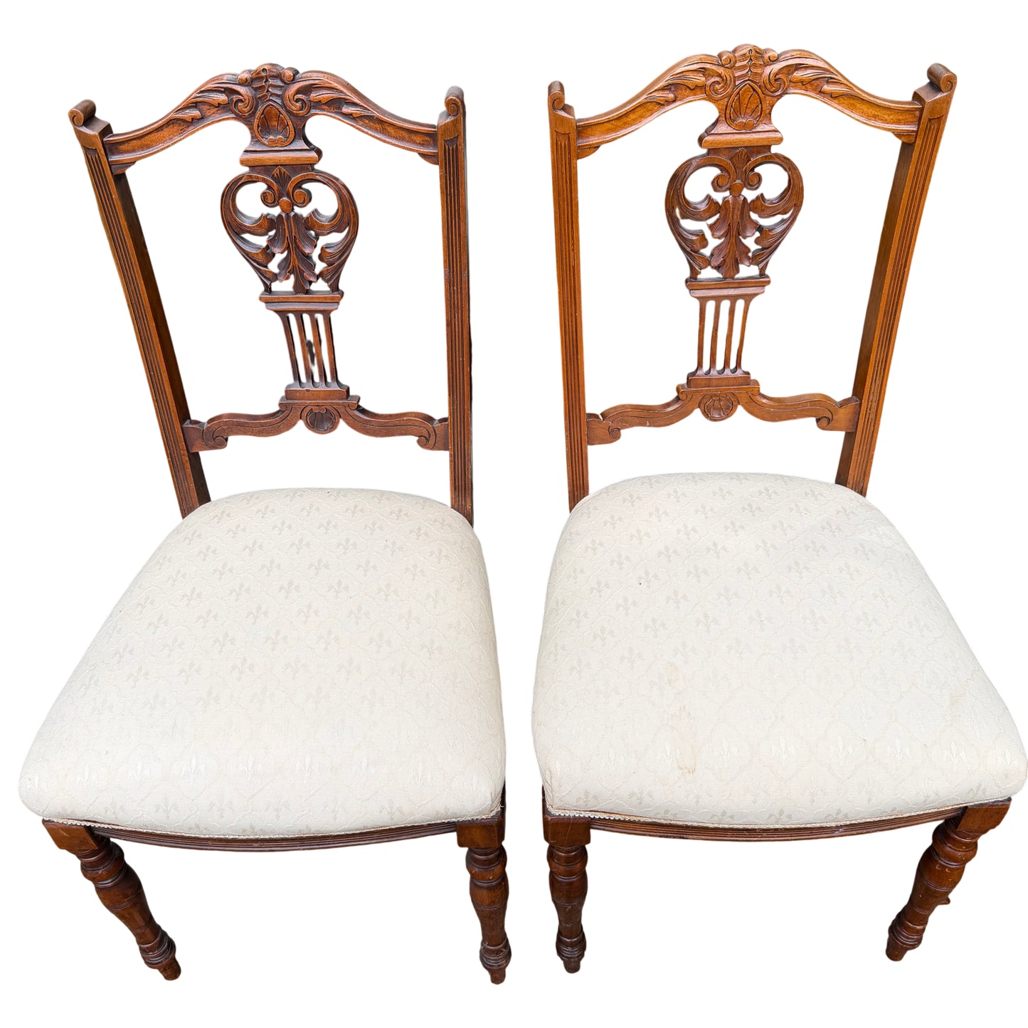 Three-quarter view of carved wooden dining chairs with cream seats and turned legs