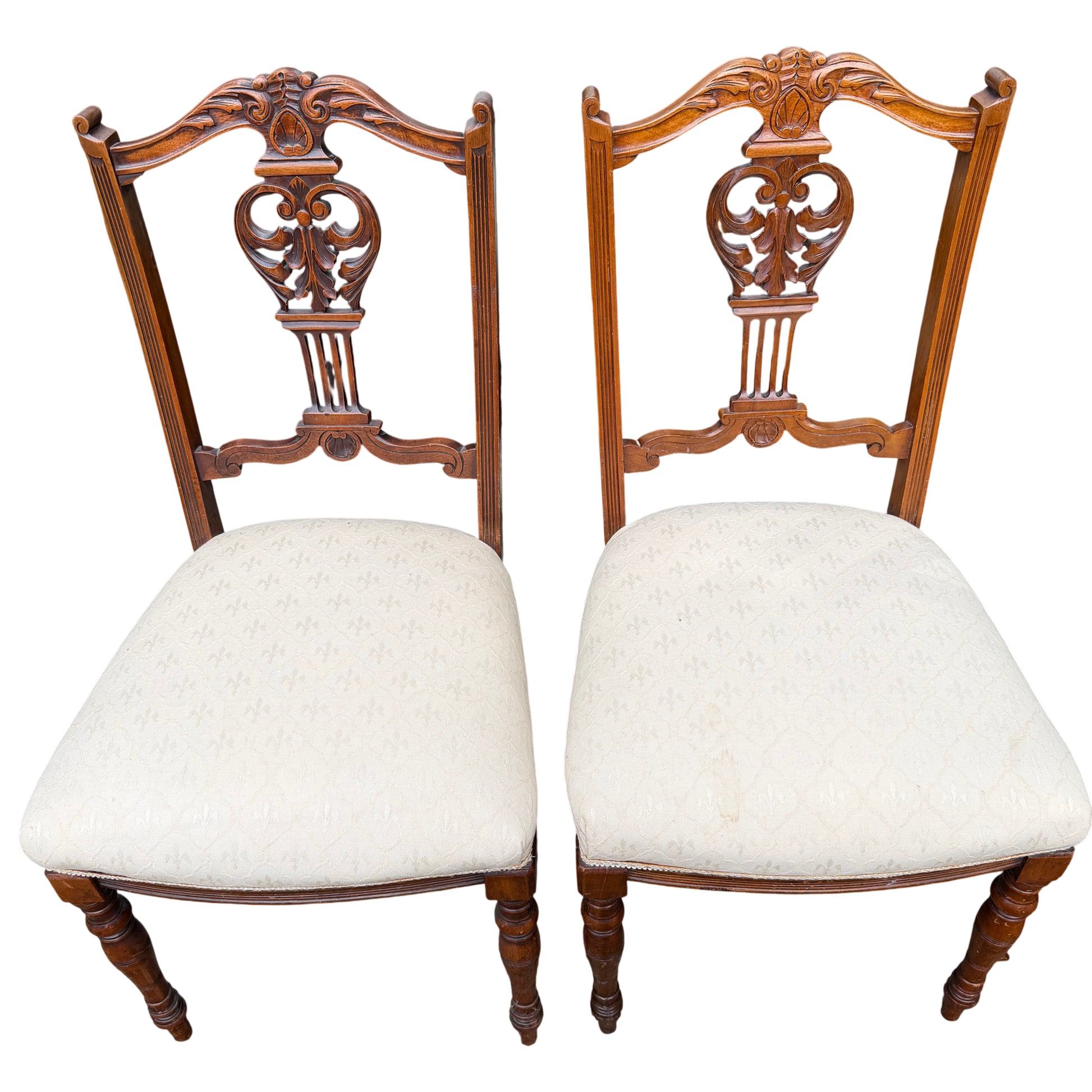 Three-quarter view of carved wooden dining chairs with cream seats and turned legs