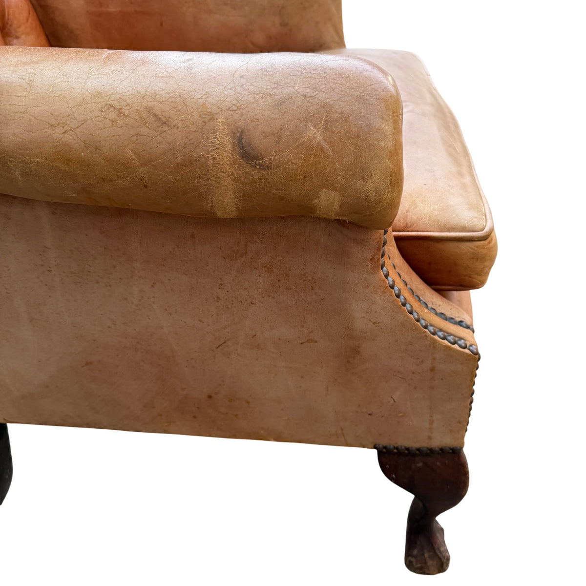 Front cabriole‑style wooden leg and foot on a vintage leather wingback chair