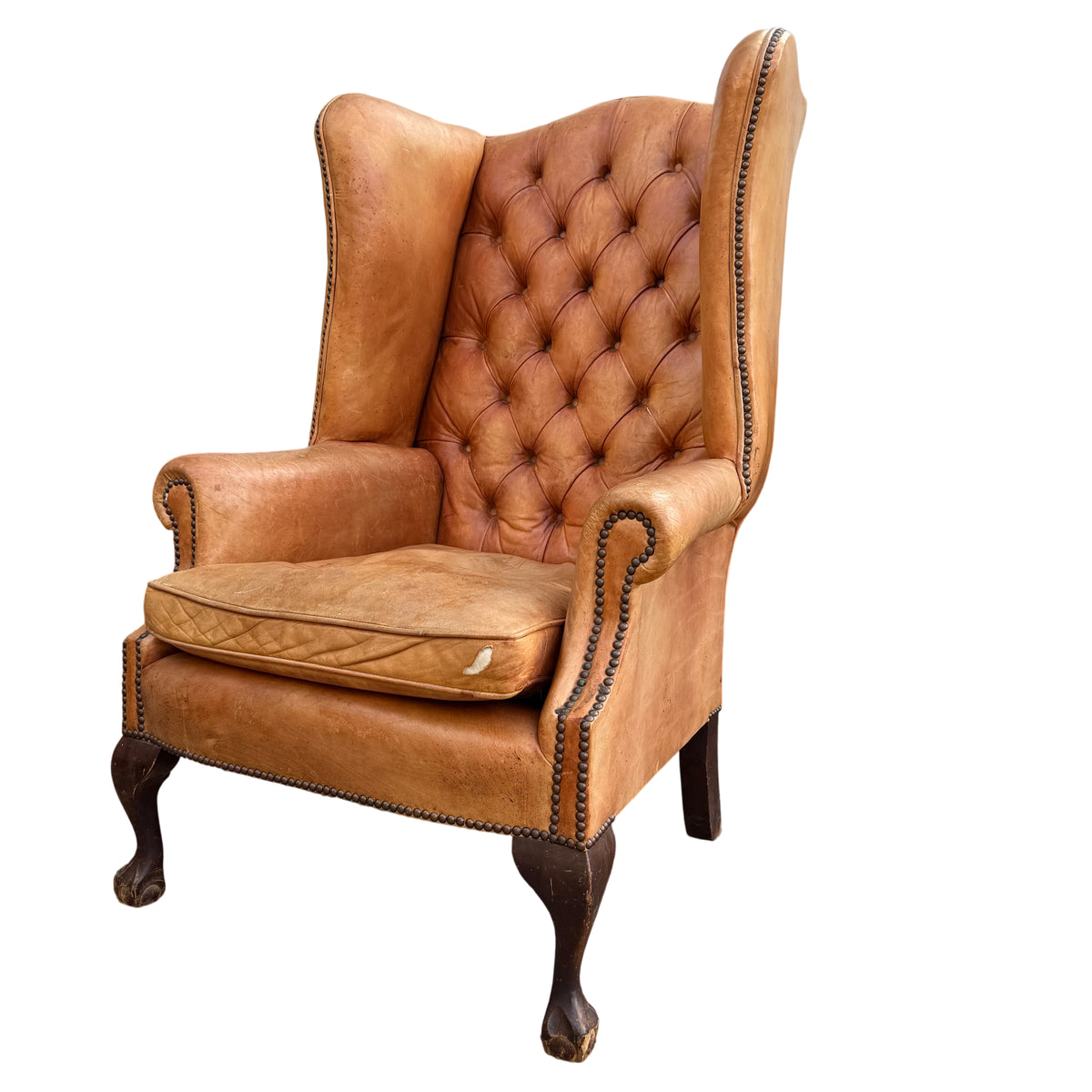 Vintage tan leather wingback armchair with deep buttoned back, brass‑coloured studding and removable cushion
