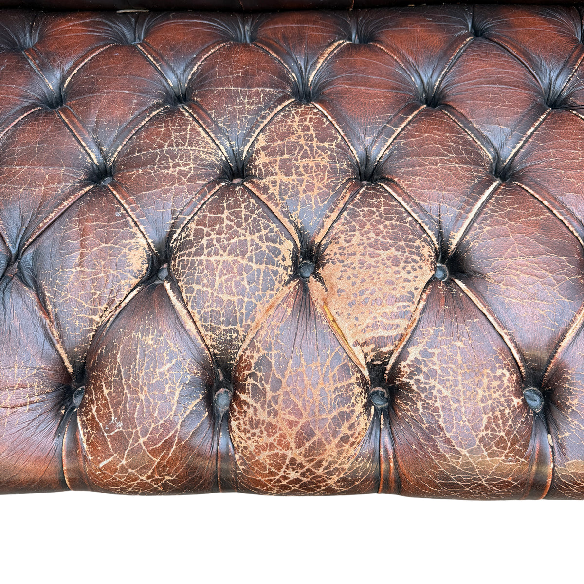 Close-up of cracked and worn leather on Chesterfield sofa seat panels