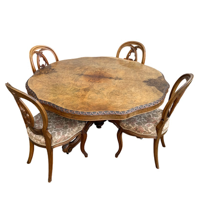 Burr walnut tilt-top dining table with carved pedestal base and four matching upholstered chairs