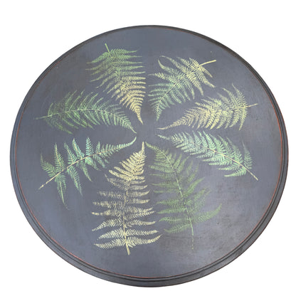 Detail of round tabletop painted with fern fronds in green and gold on dark background