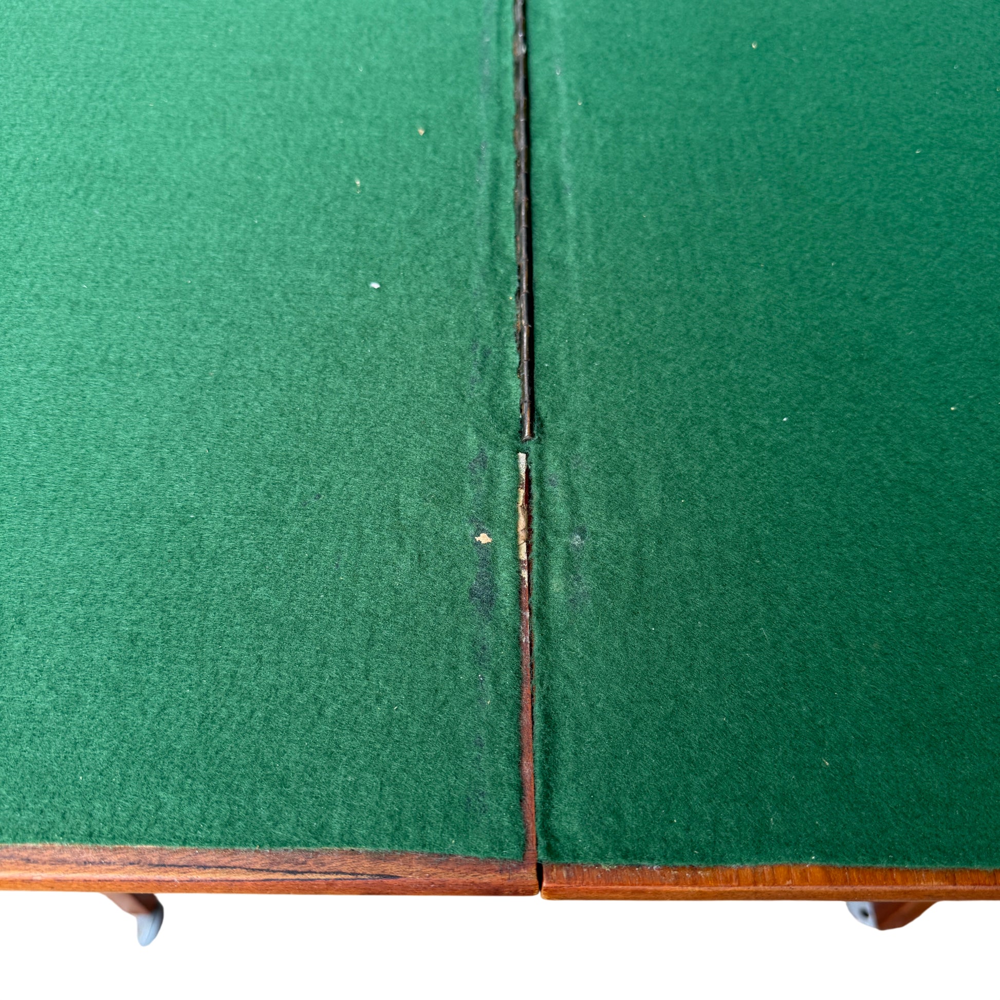 Close-up of green felt playing surface on vintage card table showing central hinge