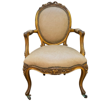 Gilt Louis-style armchair with carved wooden frame and beige faux leather upholstery, oval back and brass studs