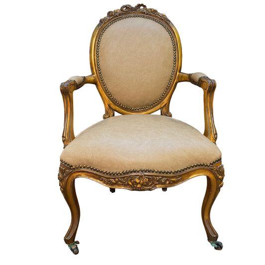 Gilt Louis-style armchair with carved wooden frame and beige faux leather upholstery, oval back and brass studs