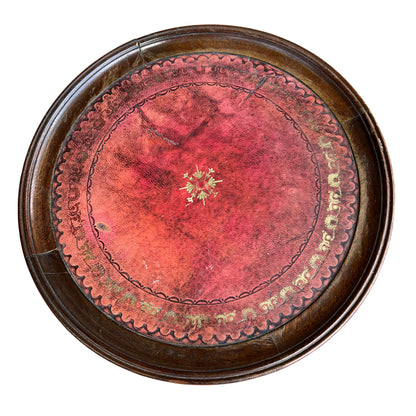 Top view of round red tooled leather inset showing decorative tooling on mahogany table