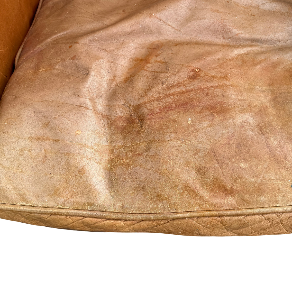 Close-up of worn tan leather seat cushion with creasing and surface cracking