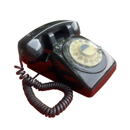 Mid century black rotary dial telephone on an orange surface