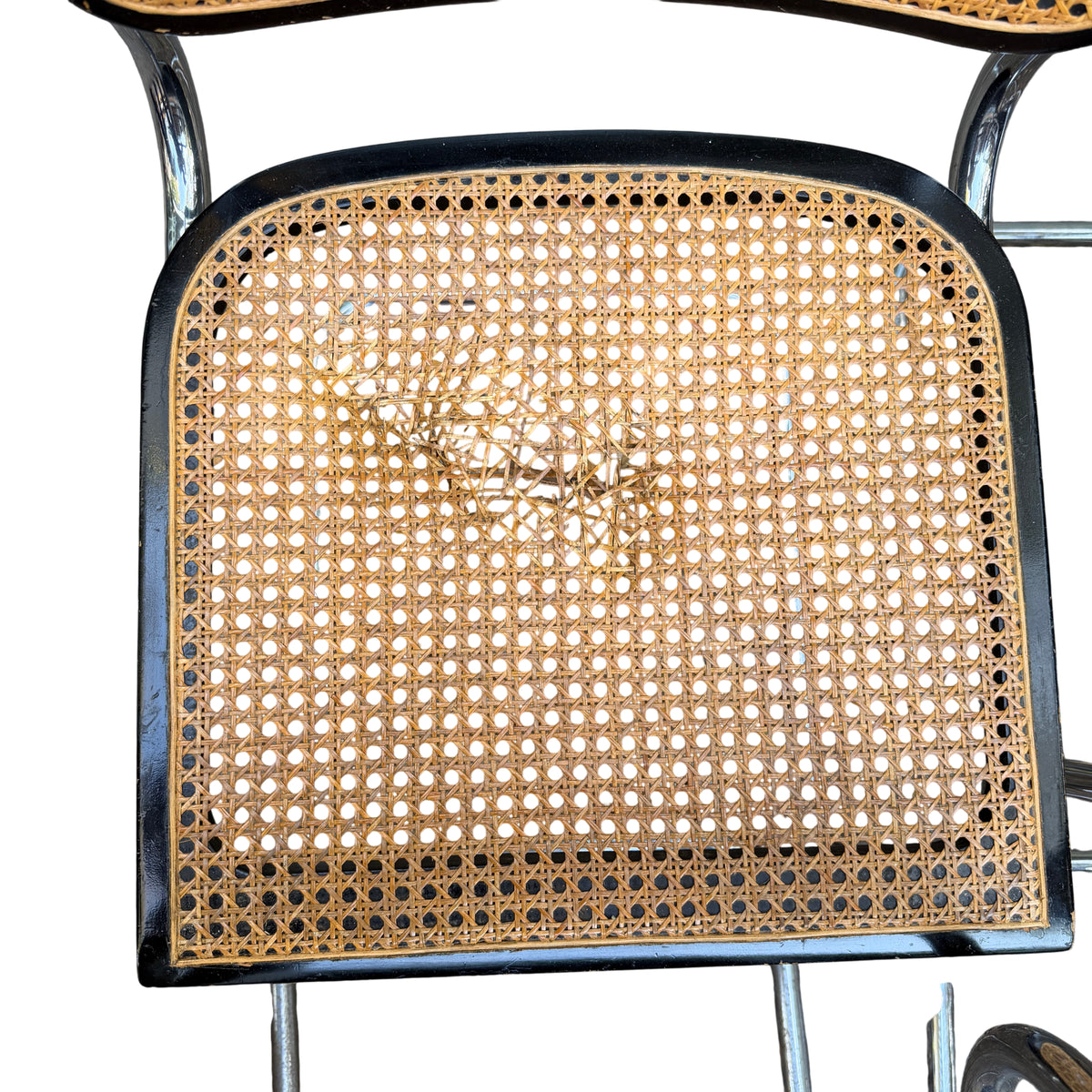 Detail of black timber surround with white paint marks and scuffs on the upper edge of a cane chair backrest