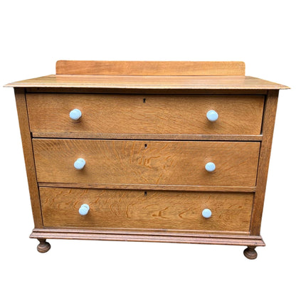 Angled view of oak chest of drawers showing turned bun feet and moulded base